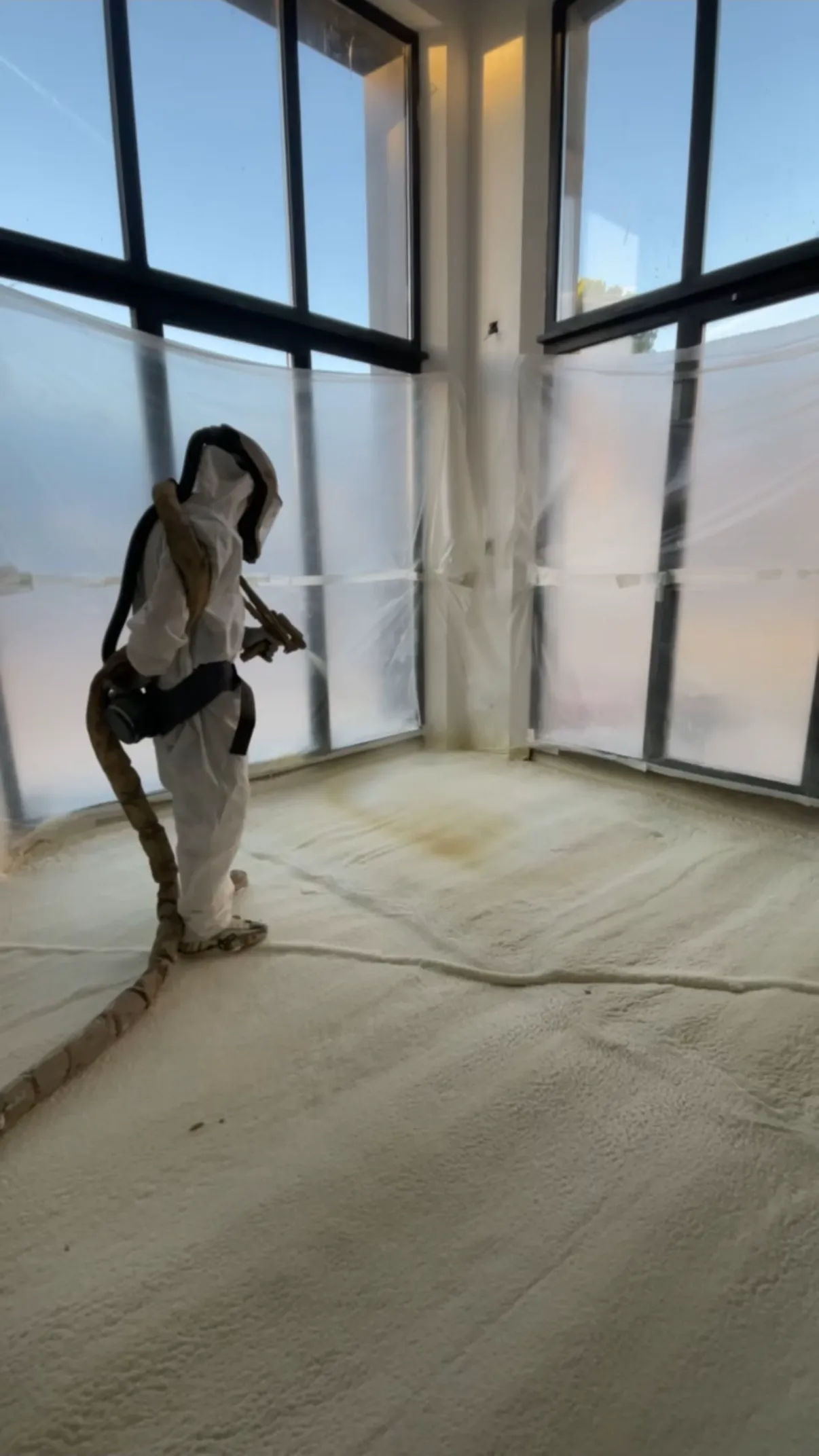 Projection de mousse polyuréthane sur un sol, devant une baie vitrée